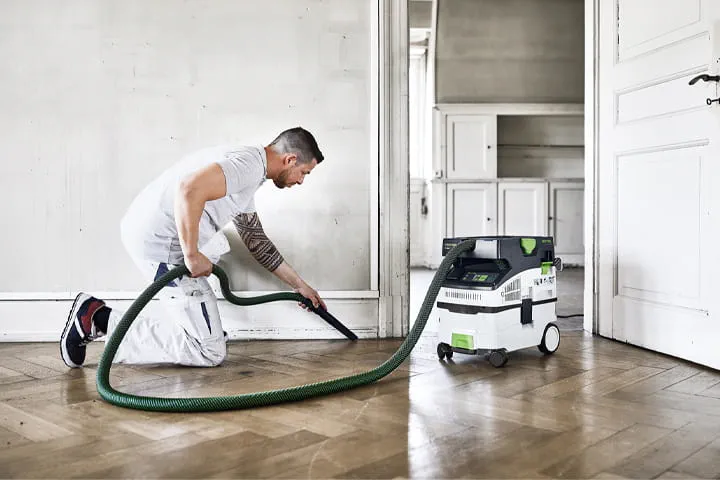Worker cleaning up job with dust extractor