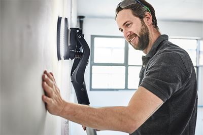 Un artisan travaille au mur avec la ponceuse à bras Planex à éclairage
